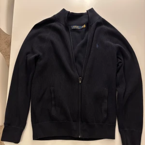 Navy full zip Polo Ralph Lauren - En mörkblå fullzip av Polo Ralph Lauren, inga slitningar, inga hål och inga defekter. Koftan är i storlek M fast sitter litet i storlek, fungerar till bägge S & M. Nypris på denna kofta ligger runt 2395, mitt pris 1999 . Är öppen för byten.