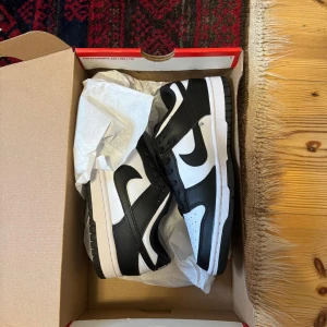 Nike Dunk i svart och vitt -NYA aldrig använda - Snygga Nike Dunk sneakers i klassisk svart och vit färgkombination. Skorna har en stilren design med snörning och den ikoniska Nike-loggan på sidan. Skorna är aldrig använda. 