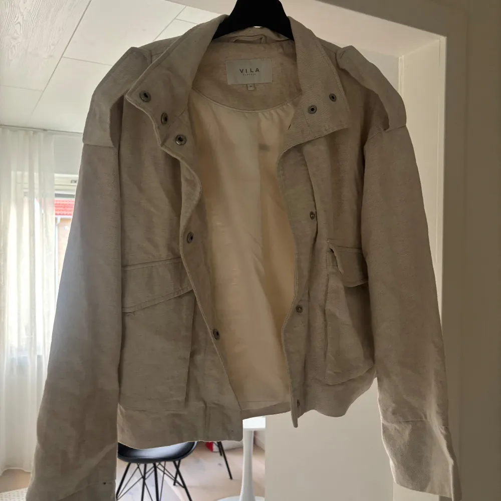 Snygg beige jacka från Vila med dragkedja och knappar. Perfekt för vår och höst med sin stilrena design och långa ärmar. Jackan har en normal passform och är tillverkad i ett bekvämt material.. Takit.