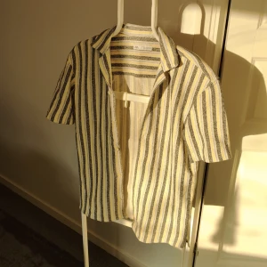 Randig kortärmad skjorta från Zara - Säljer en superfin randig skjorta från Zara i storlek S. Den har korta ärmar och ett klassiskt kragdesign. Färgerna är en mix av blått, gult, svart och vitt, perfekt för sommaren. Skjortan är i mycket bra skick och passar både till vardags och fest. Finns även matchande shorts till🌞