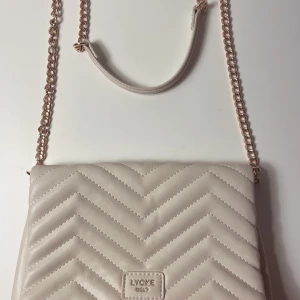 Beige quiltad axelväska från Lycke - Säljer en superfin beige axelväska från Lycke i mycket bra skick. Väskan är quiltad med ett snyggt mönster och har en avtagbar kedjerem i guld. Insidan är prickig med en praktisk dragkedjeficka. Perfekt för både vardag och fest! Mått 24x17