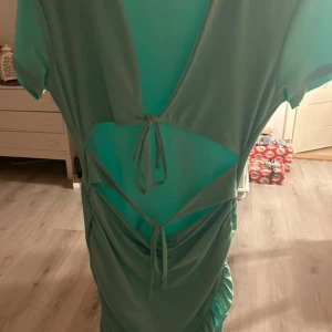 Mintgrön klänning från Shein - Snygg mintgrön klänning från Shein i ett glansigt material. Den har knytning fram och en cool cut-out design som ger en unik look. Perfekt för sommarens fester eller en utekväll. Klänningen har korta ärmar och en omlottstil med volangdetaljer.