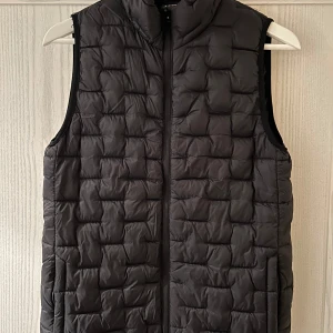 Svart dunväst från Everest - Säljer en svart dunväst från Everest i storlek 158/164. Västen har en dragkedja framtill och är perfekt för höst och vår. Den är i mycket bra skick och passar både till vardags och för utomhusaktiviteter.