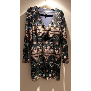 Mönstrad paljett klänning från Rebecca Stella - Snygg klänning från Rebecca Stella i storlek S. Säljer pga alldeles för liten tyvärr. Den har ett geometriskt mönster i flera färger och är täckt med paljetter. Klänningen är långärmad och har en v-ringad hals. Perfekt för festliga tillfällen!