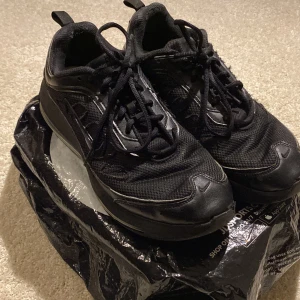 Nike Air Max - Svarta - Säljer ett par svarta Nike sneakers med snörning. Skorna har en stilren design med en diskret Nike-logga på sidan. Perfekta för en sportig look.