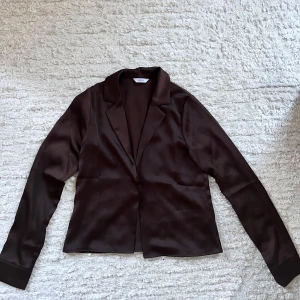 Brun skjorta från Envii - Snygg brun skjorta från Envii i ett glansigt material. Perfekt för en stilren look med klassisk krage och långa ärmar. Passar utmärkt till både vardag och fest.