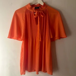 Orange blus Ralph Lauren  - En orange topp från Ralph Lauren i mycket fint skick. Toppen är plisserad och har korta ärmar. Storlek M