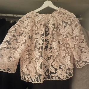 Ljusrosa spetsblus med blommönster - Säljer en superfin rosa spetsblus med blommönster. Den har en lös passform och trekvartsärmar. Blusen har knytband baktill och är i mycket bra skick då den inte är använd. 🎀