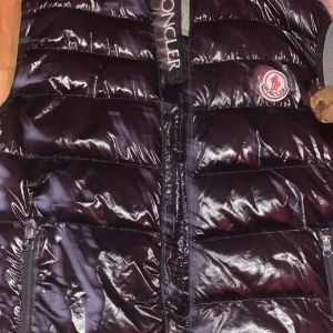 Svart dunväst från Moncler - Säljer en snygg svart dunväst från Moncler i mycket bra skick. Västen har en glansig yta med dragkedja framtill och Moncler-logga på bröstet. Perfekt för höst och vår när du vill hålla dig varm och stilren. Passar både till vardags och fest!