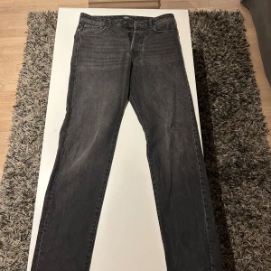 Jeans Jack & Jones  - Snygga grå jeansbyxor med en klassisk straight passform. De har en midwaist design och är perfekta för en avslappnad stil. Byxorna har en dragkedja och knappar framtill.