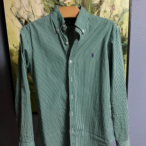 Grön randig skjorta från Polo Ralph Lauren - Säljer en snygg grön och vit randig skjorta från Polo Ralph Lauren i storlek M. Skjortan är slim fit och har långa ärmar med knappar. Perfekt för både vardag och fest! 💚