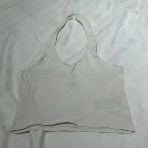 Vit topp - Vit topp som går runt nacken från H&M. Fint skick bara använd ett fåtal gånger. Ganska ostechigt material så jag tycker mer den är en XXS då jag tycker det är jobbigt att ens få på den. Skriv vid frågor eller intresse!🥰