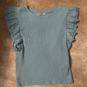 Blå ribbad topp från Zara - Säljer en superfin blå ribbad topp från Zara. Den har volangdetaljer på ärmarna som ger en söt touch. Perfekt för både vardag och fest! 💙Toppem passar även för storlek S och XS. Pris kan diskuteras!🙏🏽