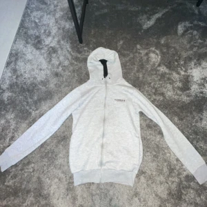 Vit hoodie med dragkedja från Horkins - Säljer en vit hoodie från Horkins i storlek M. Den har en dragkedja framtill och en mysig huva. Perfekt för kyliga dagar eller som ett extra lager. Använd men i bra skick!