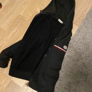 Moncler zip hoodie storlek S - Hej jag säljer min moncler hoodie för att den har blivit för liten för mig. Är rätt säker att den är äkta. Det finns två lagade hål kan skicka bild om det önskas. Helt okej skick