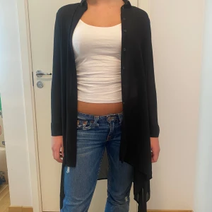 Svart lång tunn cardigan från Gina Tricot - Säljer en svart lång cardigan från Gina Tricot. Den är perfekt för lager-på-lager och har en skön, luftig passform. Cardiganen har långa ärmar och knappar framtill. Perfekt för höst och vår!