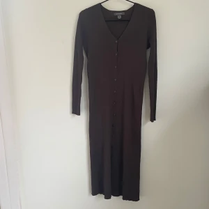 Brun långklänning med knappar/cardigan - Säljer en elegant brun långklänning med knappar hela vägen ner. Den har en v-ringad hals och långa ärmar, perfekt för höst och vinter. Materialet känns mjukt och bekvämt, vilket gör den idealisk för både vardag och festligare tillfällen. Kan även användas som cardigan