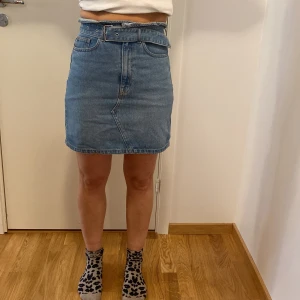 Jeanskjol från Divided - Säljer en snygg jeanskjol från Divided i storlek 36. Kjolen är i klassisk blå denim och har en medföljande bälte i midjan för extra stil. Perfekt för både vardag och festliga tillfällen. Den har en normal passform och är i nyskick. 🦋