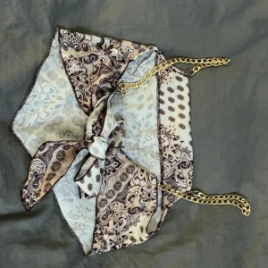 Mönstrad topp med kedjeband - Säljer en unik mönstrad topp med kedjeband i guld. Toppen har ett vackert mönster i beige och bruna toner och är perfekt för en festkväll. Den är axelbandslös och har en knytning baktill för en snygg detalj. Passar perfekt till ett par jeans eller en kjol!