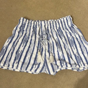 Randiga shorts från H&M - Säljer ett par superbekväma randiga shorts från H&M i blått och vitt. De har en elastisk midja med knytband och tofsar för en avslappnad look. Perfekta för sommardagar på stranden eller en chill dag hemma. 🏖️