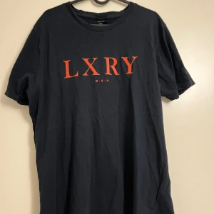 Marinblå t-shirt med orange text  - Säljer en marinblå t-shirt från new yorker med orange text på framsidan i storlek L. Den är kortärmad och i bomull, perfekt för en avslappnad stil. Passar bra till både vardag och fest. Skön och stilren design!