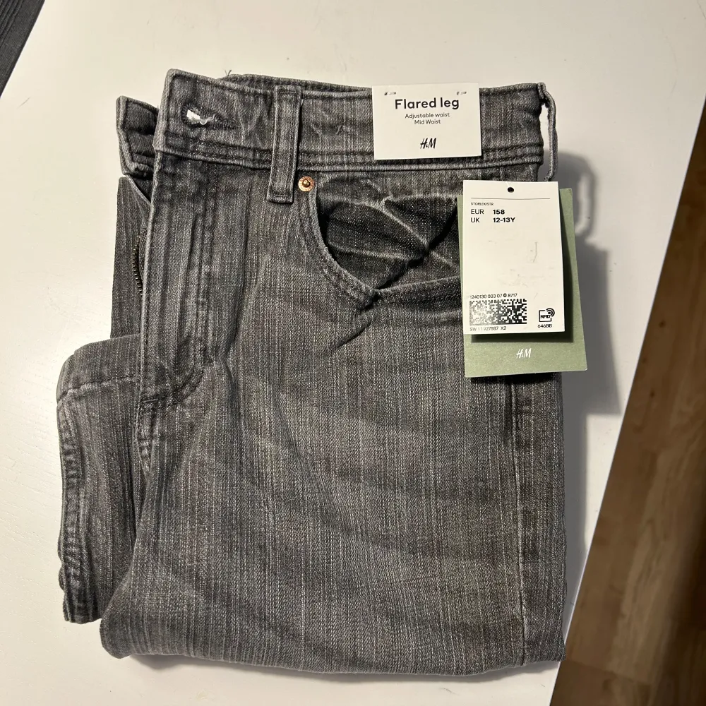 Säljer ett par snygga grå flared jeans från H&M. De har en cool vintage-look med en lätt tvättad effekt. Byxorna har en hög midja och en utsvängd bootcut-stil som ger en retro vibe. Bakfickorna är dekorerade med en söt rosett-detalj och knappar. Perfekta för både vardag och fest!. Farkut & Housut.