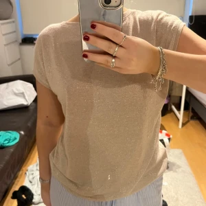 Glittrig tröja - Ljusrosa/beige tröja i glittrigt material, sticks ingenting, superfin att klä upp med kort kjol eller till jeans, man kan bära den åt båda håller, på bilden är de lite djupare urringning på ryggen