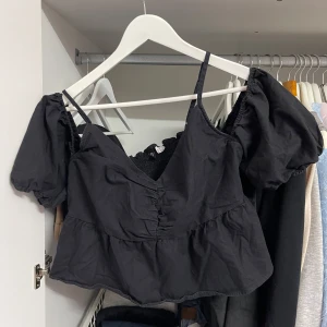 Svart offshoulder topp från H&M Divided - Säljer en superfin svart offshoulder topp från H&M Divided. Den har puffiga korta ärmar och en smockad detalj på ryggen som ger en skön passform. Perfekt för både vardag och fest! 🖤
