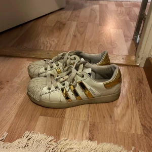 Adidas Superstar i vitt och guld - Unika Adidas Superstar sneakers i vitt med guldiga detaljer. Ser väldigt smutsiga ut på bilden men är i bättre skick i verkligenheten 