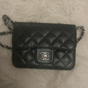 Svart väska  - Snygg svart quiltad axelväska med kedjedetaljer och logotyp på framsidan. Röd inuti väskan 