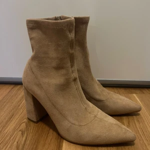 Beige mocka boots med klack - Snygga beige boots i mocka med spetsig tå och klack. De har en praktisk dragkedja på sidan för enkel på- och avtagning.