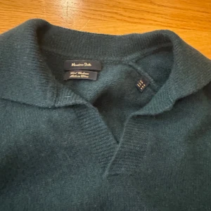 Mörkgrön tröja från Massimo Dutti - Säljer en stilren mörkgrön tröja från Massimo Dutti. Tröjan har en klassisk krage och långa ärmar med ribbade muddar. Perfekt för en elegant och avslappnad look.