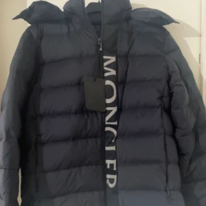  Moncler Ume - Snygg svart dunjacka från Moncler med dragkedja och hög krage. Jackan har en stilren design med Moncler-logga längs dragkedjan. Perfekt för kyliga dagar. Storlek M passar L pris kan diskuteras 