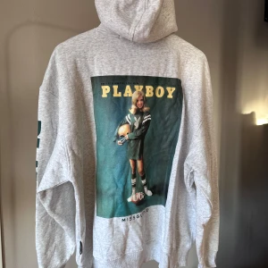 Grå hoodie med Playboy-tryck från Missguided - Snygg grå hoodie med dragkedja och stort Playboy-tryck på ryggen. Framsidan har en liten Playboy-logga och text på ärmen. Perfekt för en avslappnad stil.