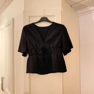 Svart volang blus med knytning  - Snygg svart volang topp från SHEIN med v-ringning och knytning i midjan. Endast använd 1 gång