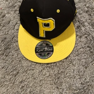 Svart och gul keps med broderad bokstav - Snygg svart keps med gul skärm och broderad bokstav 'P' framtill. Perfekt för en sportig look eller som en cool accessoar till vardagsoutfiten.