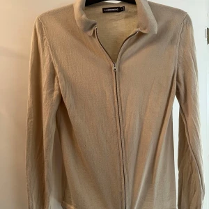 Beige cardigan från J.Lindeberg - Snygg beige cardigan från J.Lindeberg i merinoull. Tröjan har en dragkedja framtill och långa ärmar, perfekt för lager på lager-stil. Passar bra till både vardag och mer uppklädda tillfällen.