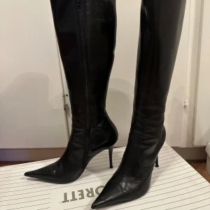 Svarta stövletter med klack - Eleganta svarta stövletter i skinn med spetsig tå och hög klack. De har en praktisk dragkedja på sidan för enkel på- och avtagning. Perfekta för en stilren look.