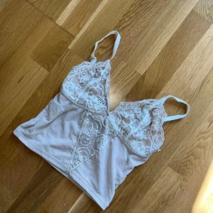 Beige spetslinne från Bik Bok - Säljer ett snyggt beige linne från Bik Bok med spetsdetaljer. Linnet har smala axelband och en v-ringad design med spets över bysten. Använd ett par gånger men blivit för liten. Fint skick