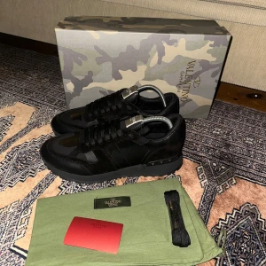 Svarta sneakers från Valentino Garavani - Snygga svarta sneakers från Valentino Garavani med kamouflagemönster. Skorna har snörning och en stilren design. Perfekta för en trendig look.