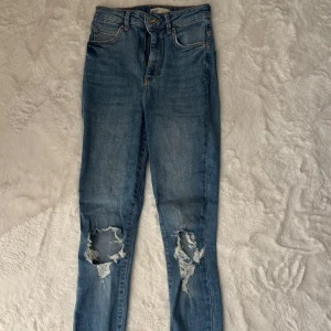 Jeans med slitningar - Jeans från GinaTricot men ovetandes av modell. Står ej på jeansen. Skinny fit med hög midja. Alla hål och slitningar är enligt modellen, inte själv gjorda. Använda enstaka gånger och är i mycket bra skick utan inga vidare tecken på användning. Stretchiga i storlek 34