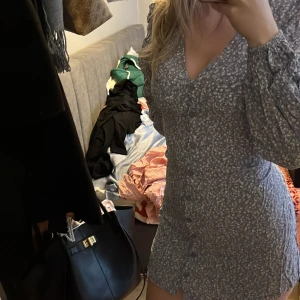 Blommig klänning från Nelly - Söt blommig klänning från Nelly i blått med små vita blommor. Klänningen har långa ärmar och knappar framtill, perfekt för en avslappnad stil.