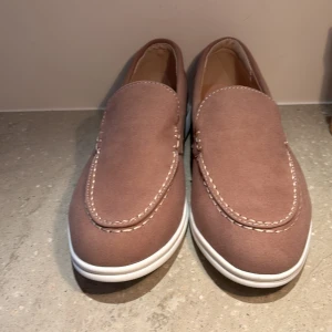 Bruna loafers med vit sula - Snygga bruna loafers med kontrasterande vit sula. Skorna har en stilren design med dekorativa sömmar och är perfekta för en avslappnad look. Endast testade inomhus