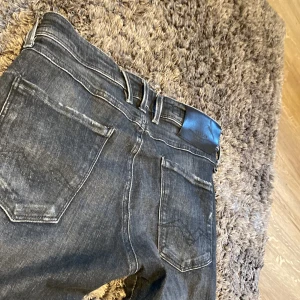 Replay Anbass jeans i mörk tvätt - Snygga Replay Anbass jeans i mörk tvätt med slim fit passform. Tillverkade av ekologisk bomull för en skön känsla. Klassisk femficksdesign med knappgylf och bälteshällor.
