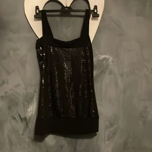 Svart paljetttopp -   Strl S/M Snygg svart topp med paljetter framtill som ger en glittrig effekt. är ärmlös , perfekt för festliga tillfällen.