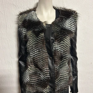 Zebramönstrad pälsjacka med skinnärmar - Säljer en unik jacka med zebramönstrad päls framtill och quiltade skinnärmar. Jackan har en cool kombination av material och mönster som verkligen sticker ut. Perfekt för dig som vill ha något annorlunda i garderoben!