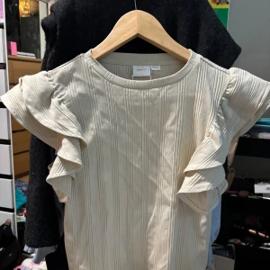 Beige ribbad topp från Gina Tricot - Säljer en stilren beige ribbad topp från Gina Tricot med volangdetaljer på ärmarna. Perfekt för en trendig look. 🧡