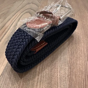 Blått flätat bälte med silverdetaljer - Snyggt blått flätat bälte med silverfärgat spänne och bruna läderdetaljer. Perfekt för att ge en stilren touch till din outfit. Bältet är flexibelt och passar de flesta storlekar.