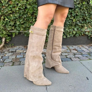 Beige mockastövlar med dragkedja - Snygga beige stövlar i mocka med dragkedja på sidan och en dekorativ spänne upptill. De har en spetsig tå och är perfekta för höst och vår. De är endast använda en gång.