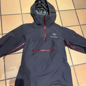 Svart vindjacka från Arc'teryx - Säljer en svart vindjacka från Arc'teryx med GORE-TEX Paclite Shell. Jackan har flera praktiska dragkedjor i rött. Perfekt för utomhusaktiviteter och skyddar mot väder och vind.